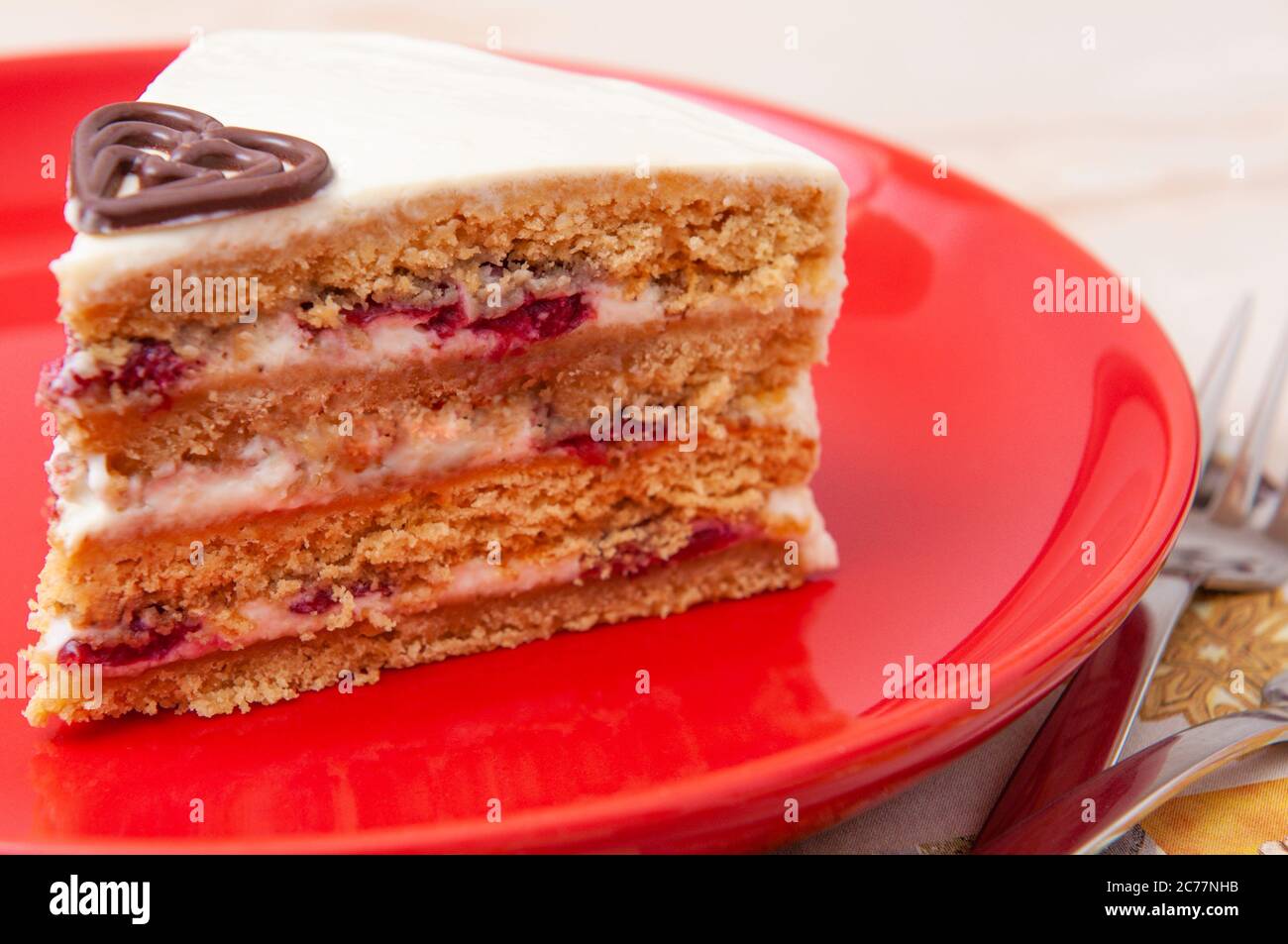 Fetta di torta bianca con quattro strati su un piatto rosso con decorazione a forma di cioccolato Foto Stock