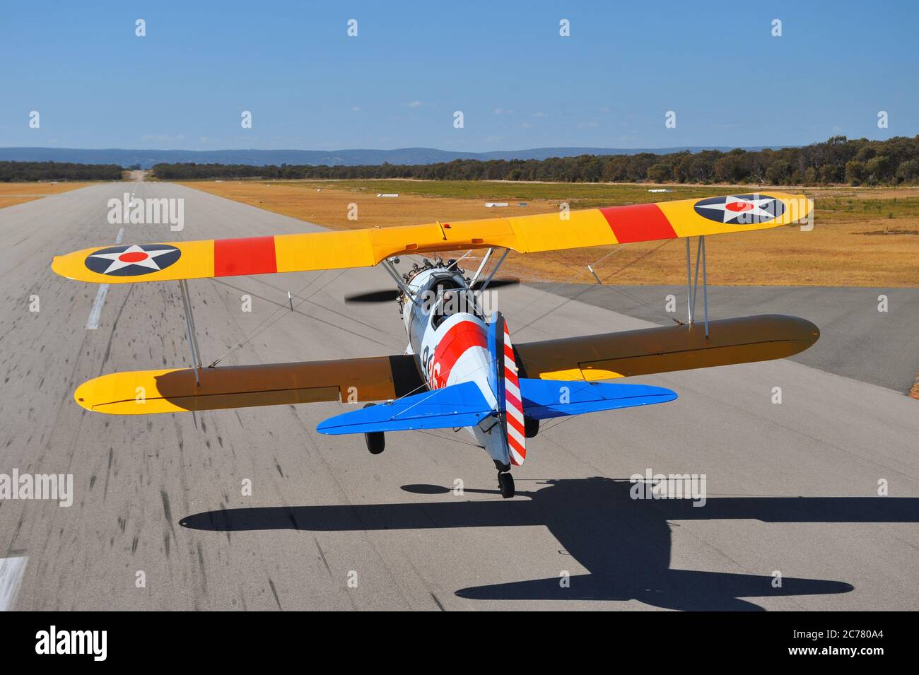 Un ritratto dall'aria all'aria con vista posteriore, di un addestratore biplano restaurato del Boeing Stearman della Marina degli Stati Uniti degli anni '40 che atterra in un campo aereo. Foto Stock