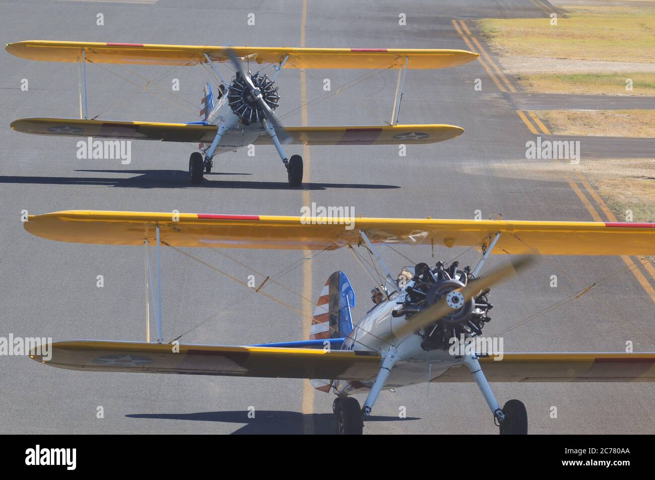 Un ritratto da aria a terra, di due addestratori biplanari restaurati della Marina militare americana Boeing Stearman degli anni '40 che tassano in un campo aereo. Foto Stock