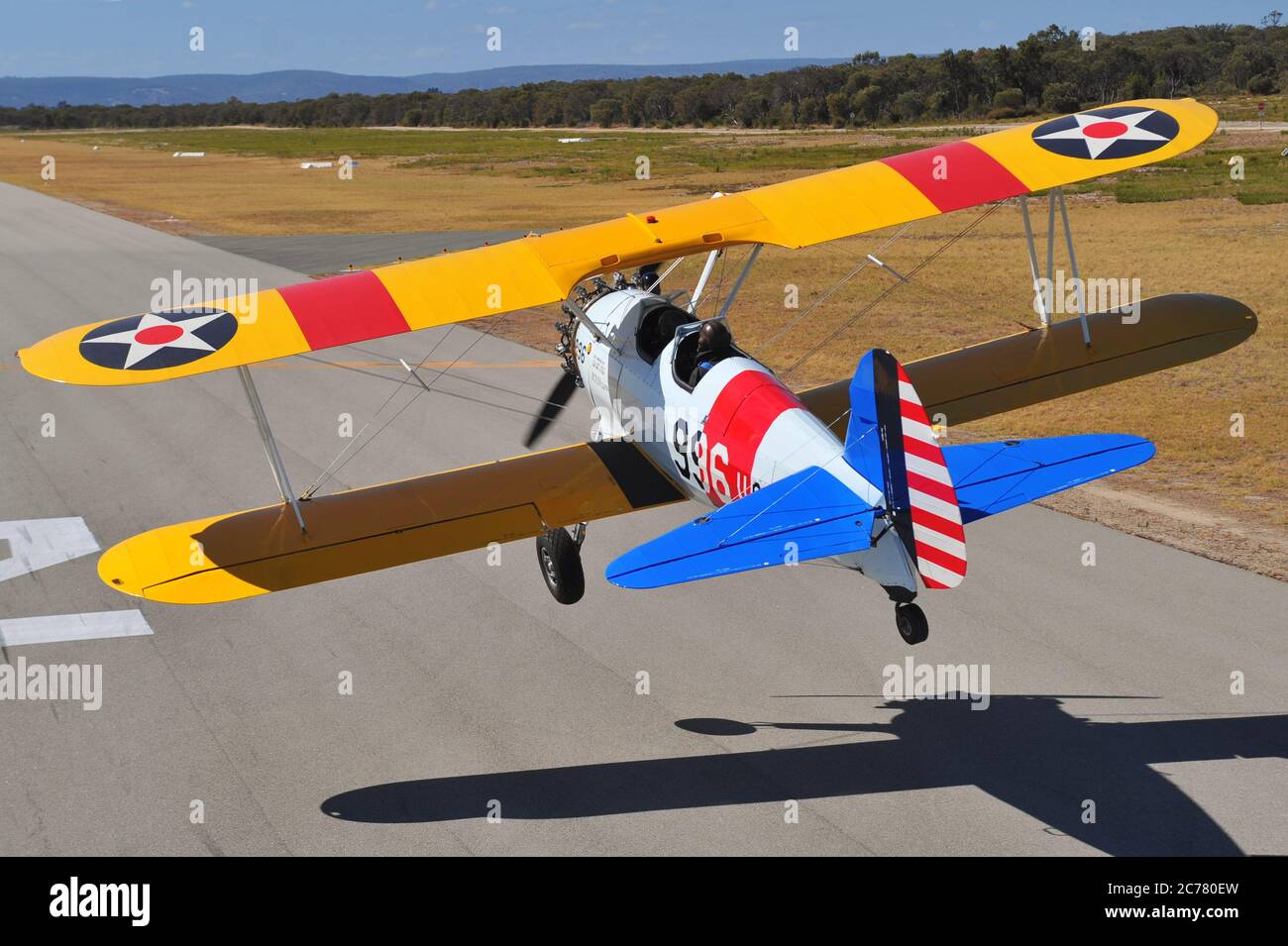 Un ritratto dall'aria all'aria con vista posteriore, di un addestratore biplano restaurato del Boeing Stearman della Marina degli Stati Uniti degli anni '40 che atterra in un campo aereo. Foto Stock