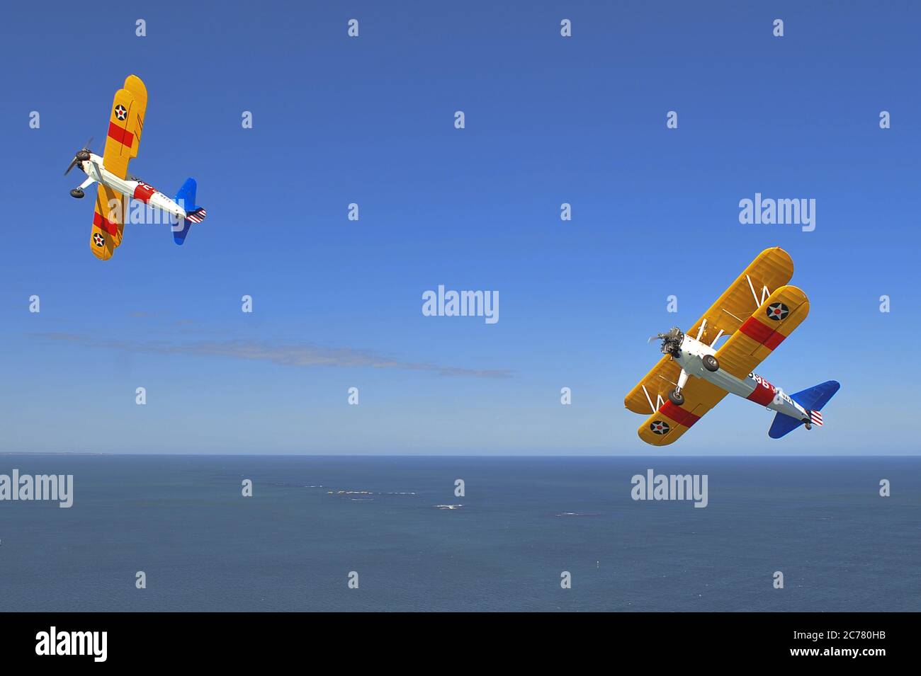 Un ritratto aria-aria di due addestratori biplanari Stearman della Marina statunitense Boeing N2S degli anni '40 restaurati che si arrampicano, con uno sfondo oceanico. Foto Stock