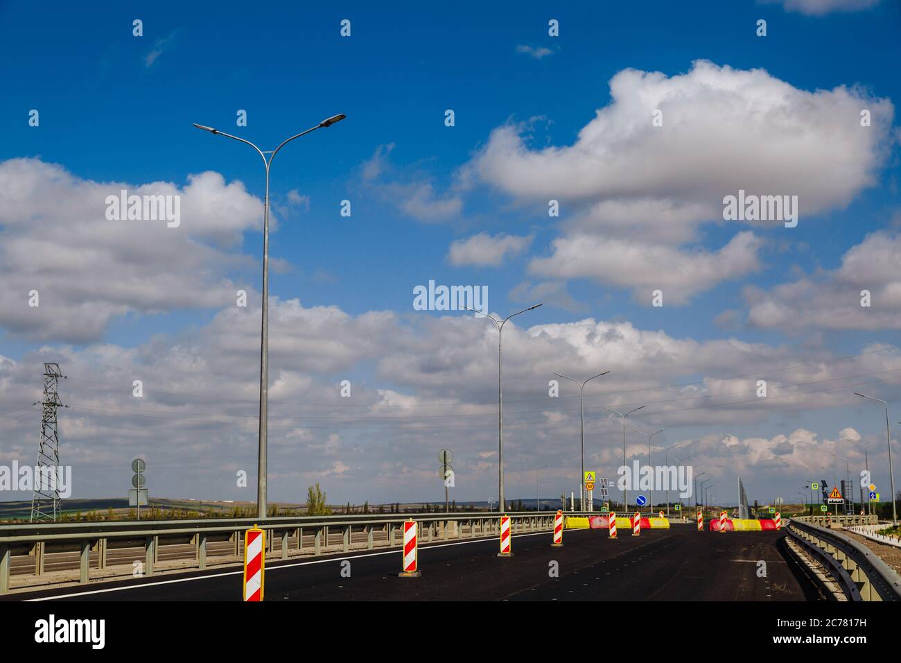 Nuova strada asfaltata con luci da strada su sfondo di cielo blu con nuvole bianche. Foto Stock