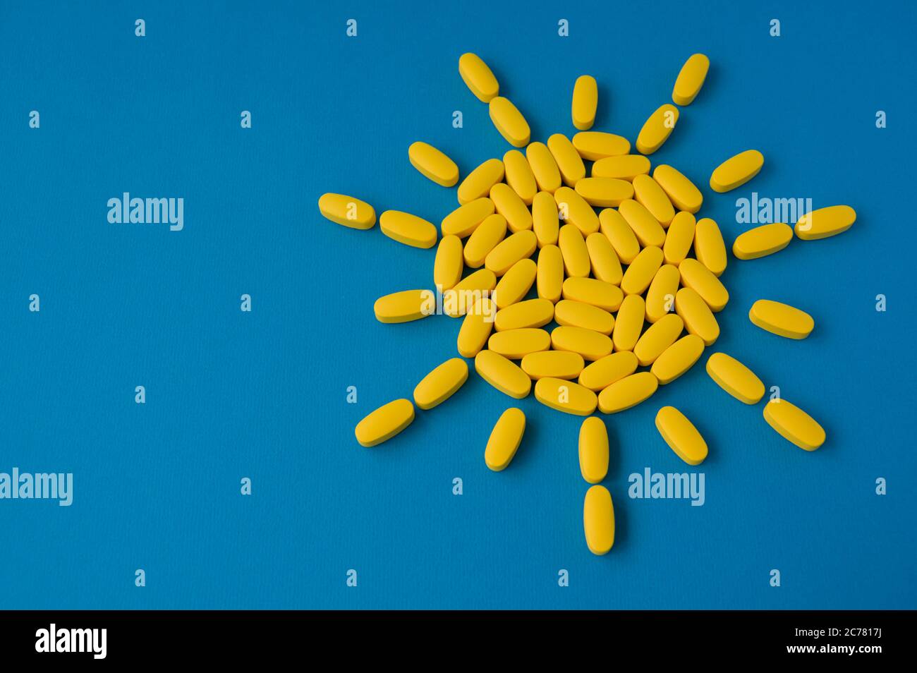 Concetto di vitamina D del sole giallo estivo da compresse pillole su superficie blu con spazio di copia Foto Stock