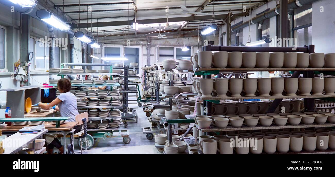 Boleslawiec, bassa Slesia, Polonia., scaffali in un'affollato studio di ceramica pieno di lavori finiti e pezzi di argilla che asciugano sotto il controllo di una donna Foto Stock