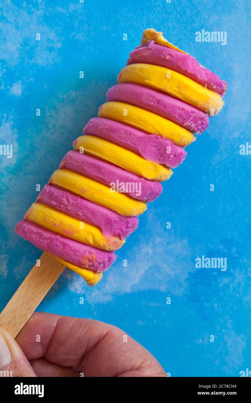 Tenendo la insalata di frutta Barratt Raspberry & Pineapple Flavour Ice Lolly su sfondo blu a motivi geometrici Foto Stock