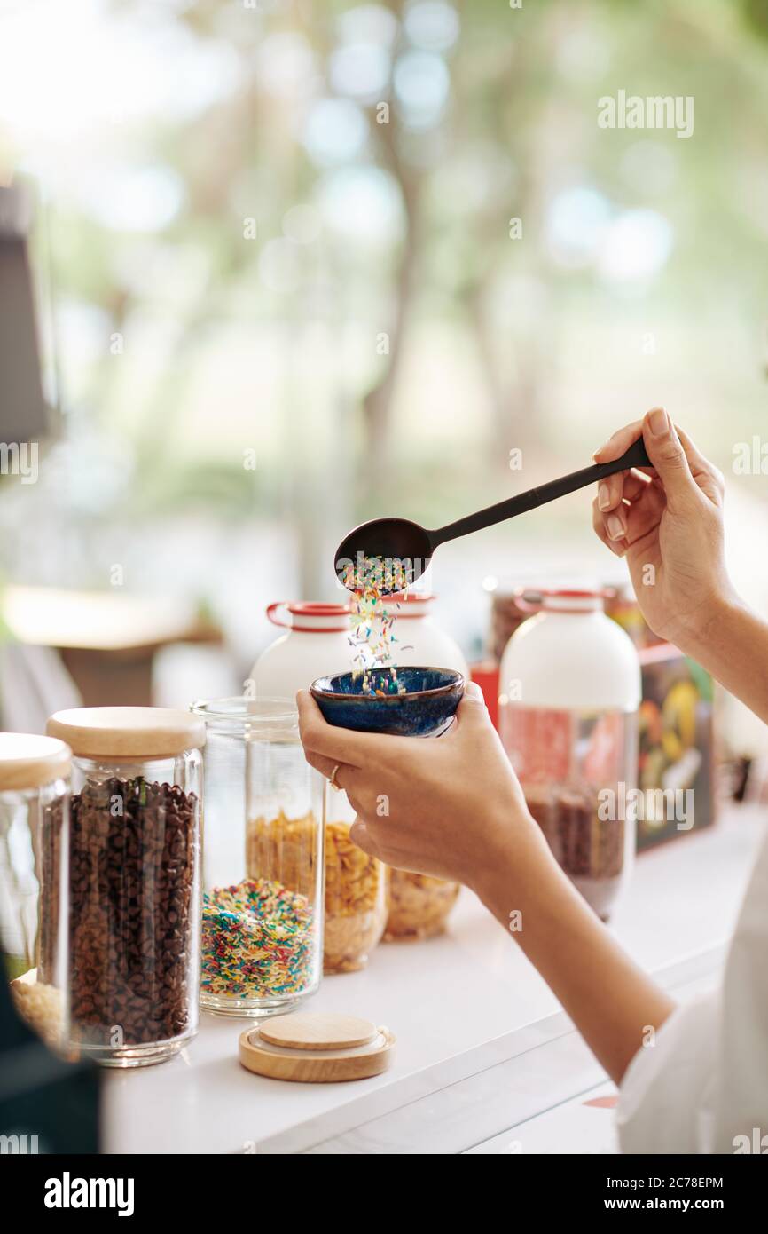 Mano del cameriere mettendo un cucchiaio grande di spruzzette in ciotola con gelato per il cliente Foto Stock