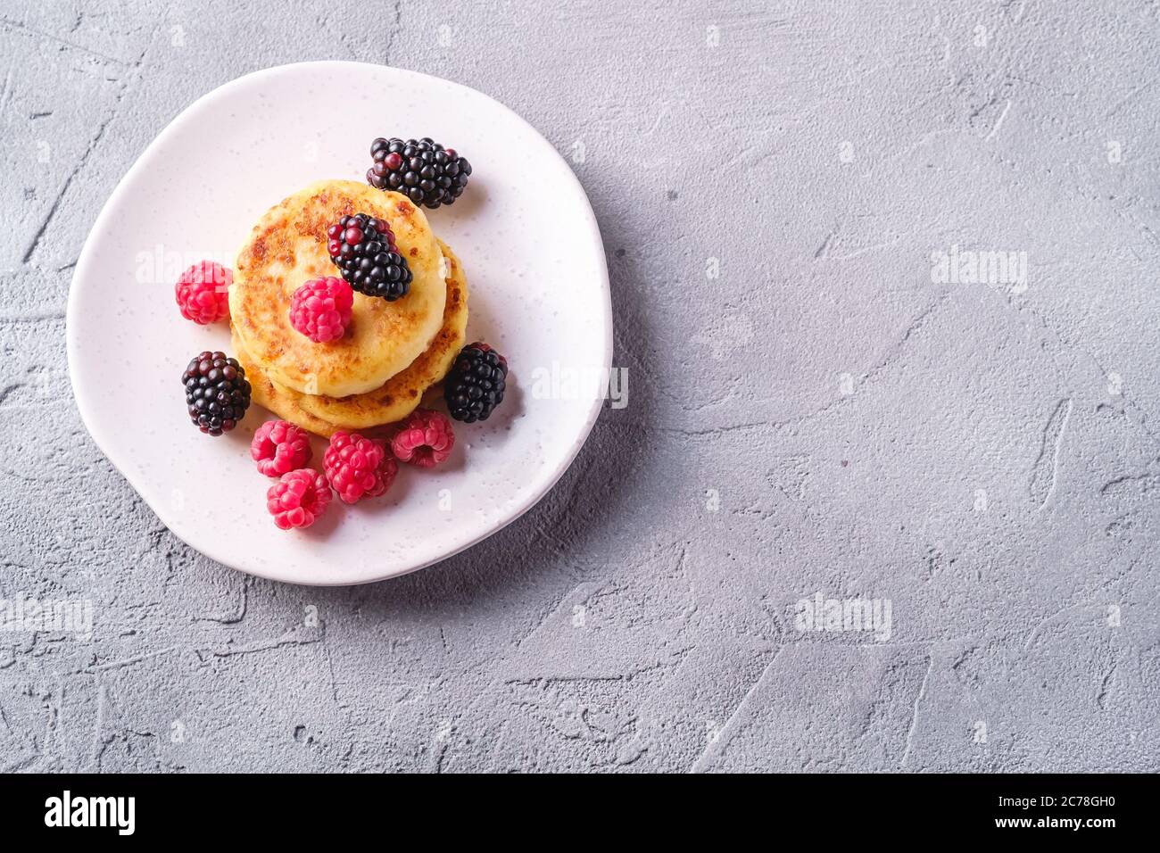Frittelle al formaggio, frittelle di cagliata dessert con lampone e frutti di mora in piastra su fondo di pietra in cemento, spazio copia vista dall'alto Foto Stock
