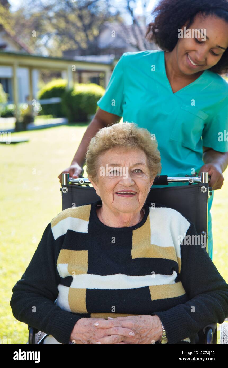 Donna che assiste la donna anziana sulla sedia a rotelle. Foto Stock