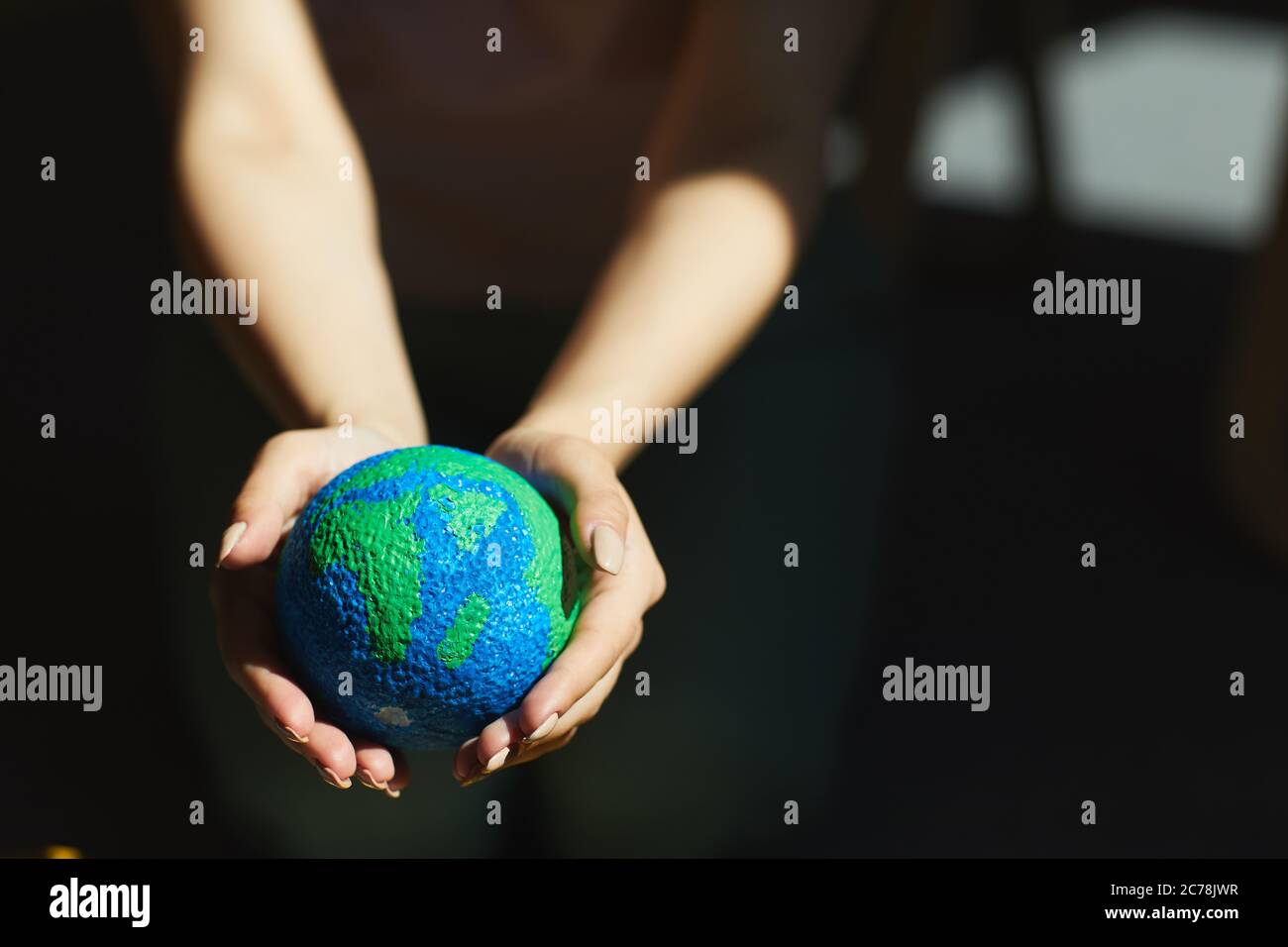 Primo piano di una donna irriconoscibile che tiene il modello del pianeta in mani alla luce del sole, salvando il concetto della Terra Foto Stock