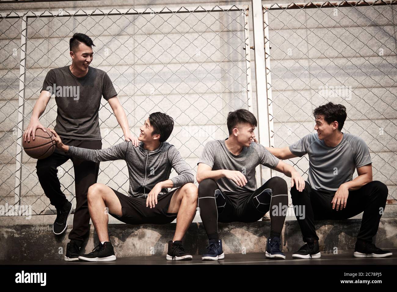 gruppo di quattro giovani adulti asiatici che riposano mentre chiacchierano sul campo da pallacanestro all'aperto Foto Stock