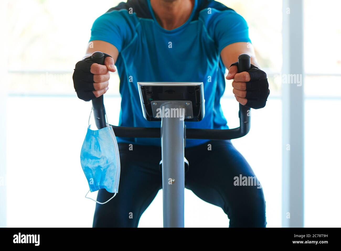primo piano di un giovane caucasico in palestra, indossando abbigliamento sportivo, utilizzando una cyclette, e la sua maschera chirurgica che tiene dal manubrio mentre è no Foto Stock