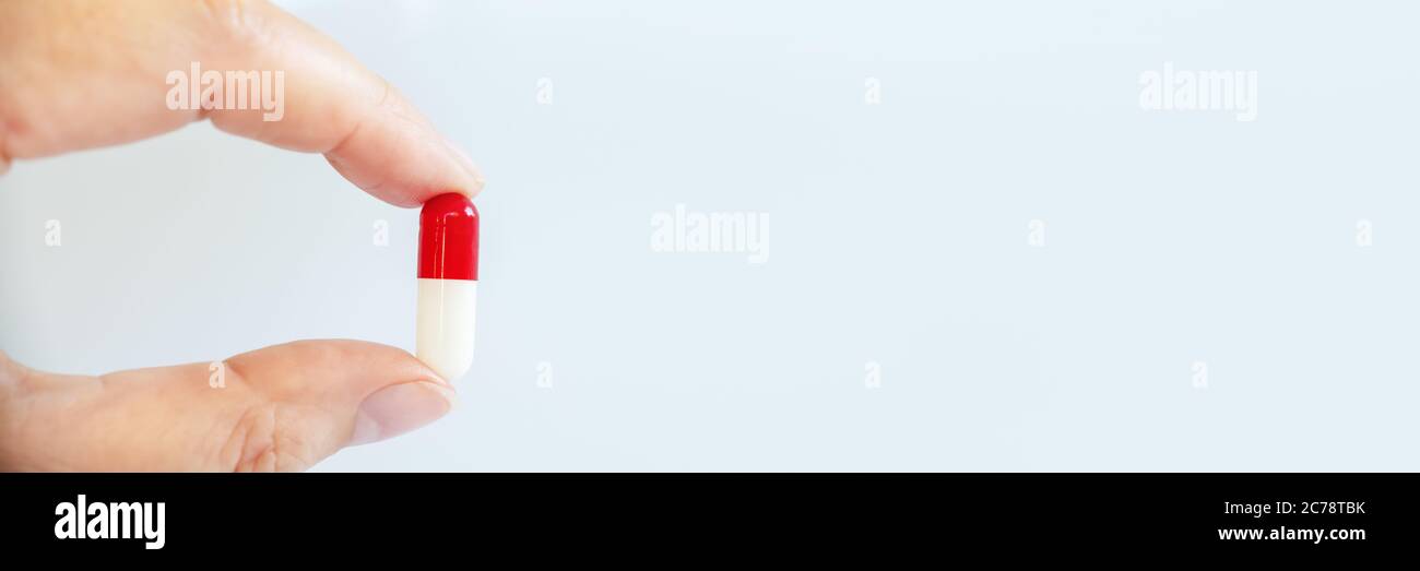 Primo piano di una mano che tiene una pillola bianca e rossa, salute e banner web di farmaci Foto Stock