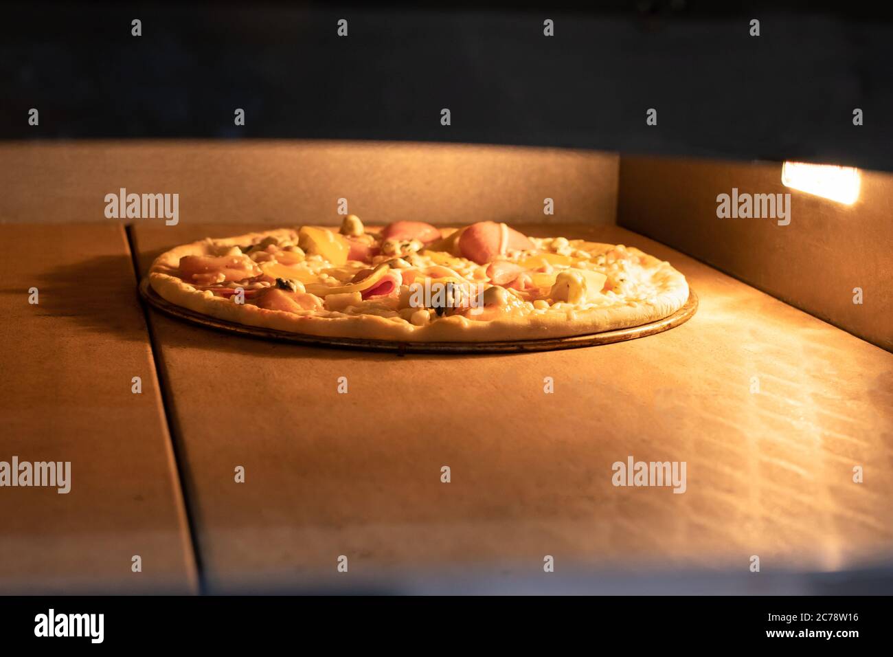 La pizza viene cotta nel forno. Il processo di cottura della pizza italiana, forno, alta temperatura. Pizza con pollo, pomodori e formaggio Foto Stock