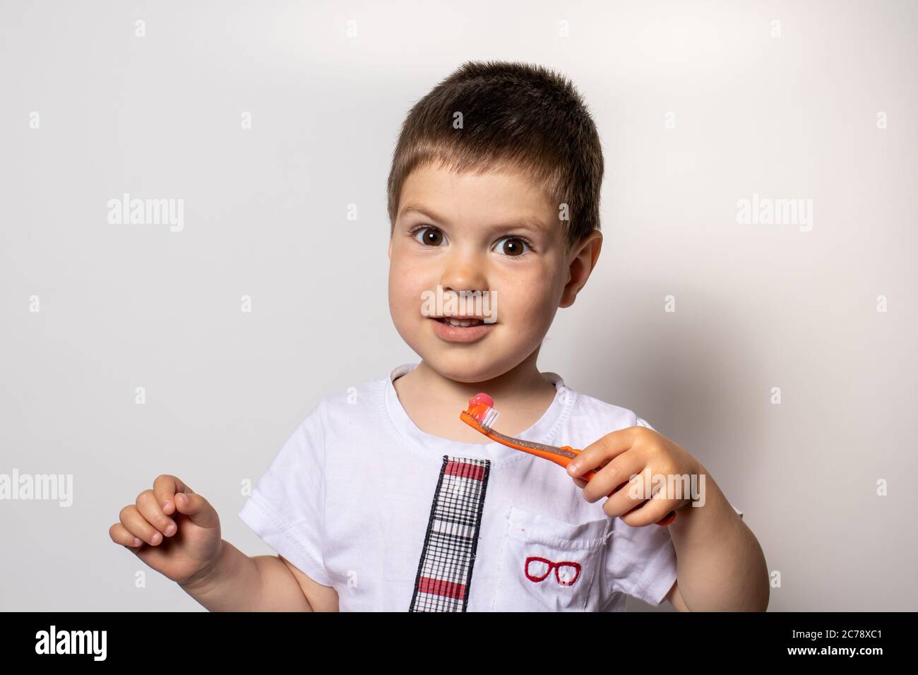 Un bambino tiene uno spazzolino arancione con dentifricio. Il bambino pennellerà i denti, prevenendo la carie dei denti Foto Stock