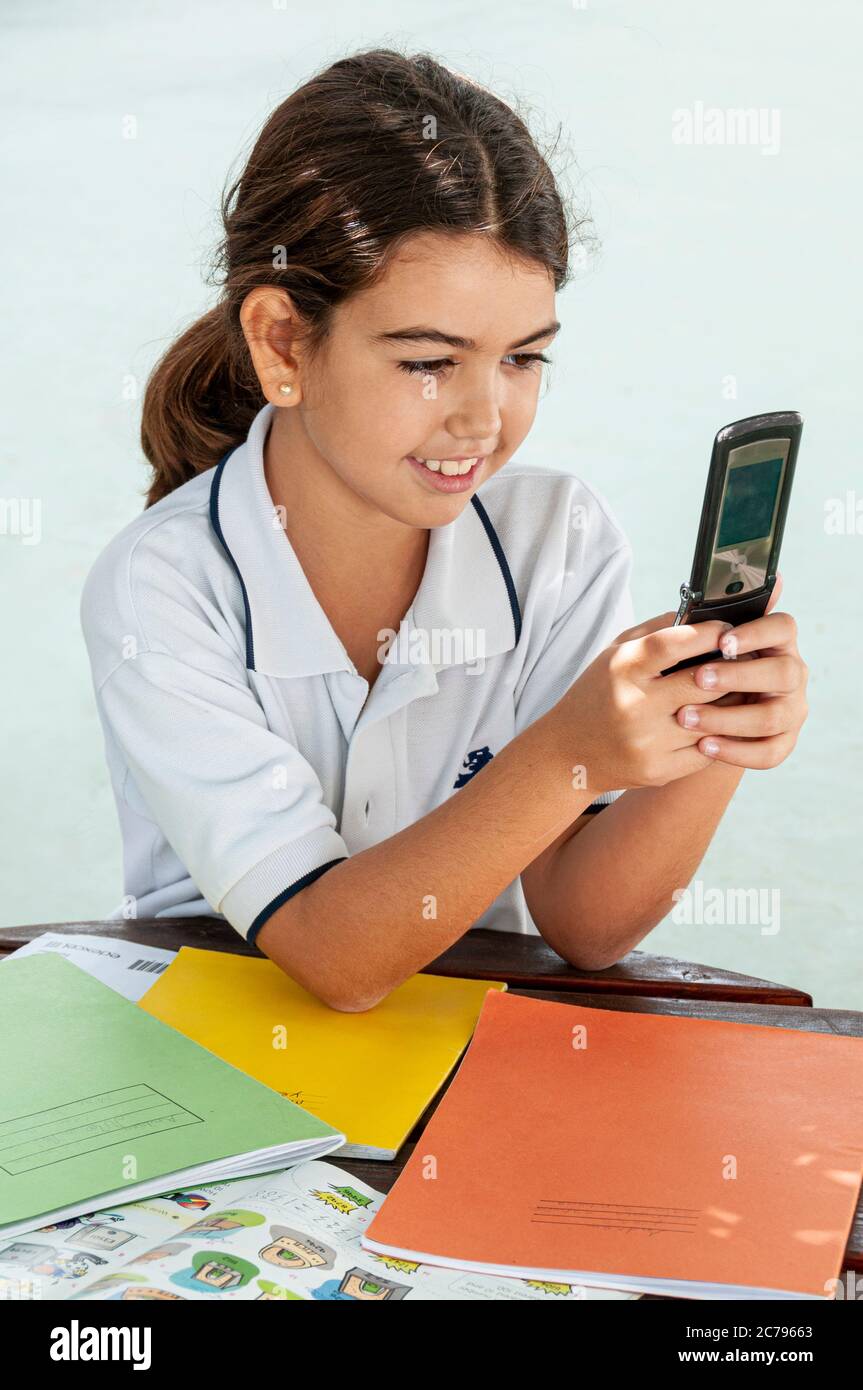 Flip Phone vecchia tecnologia Motorola scolastica junior 7-9 anni all'aperto studiare in un parco giochi scuola soleggiato utilizzando cellulare per SMS Foto Stock