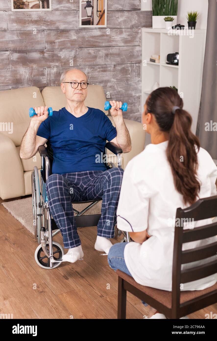 Medico che spiega gli esercizi a una persona anziano in sedia a rotelle. Disabili anziani disabili con lavoratore sociale in recupero terapia di supporto fisioterapia sistema sanitario di cura casa di riposo Foto Stock