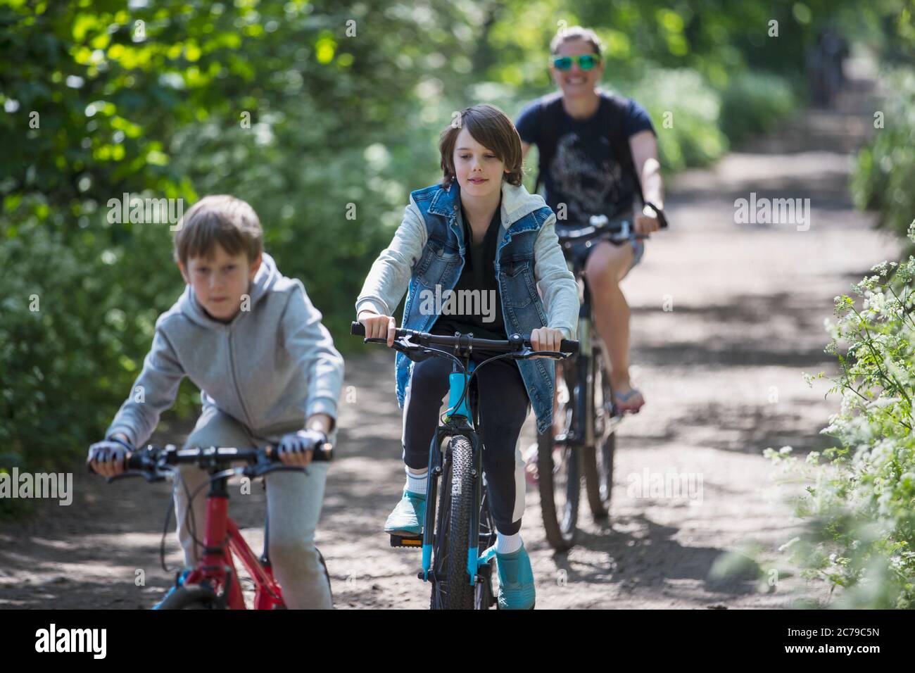 Madre e figli che si divertano in bicicletta su un sentiero soleggiato Foto Stock