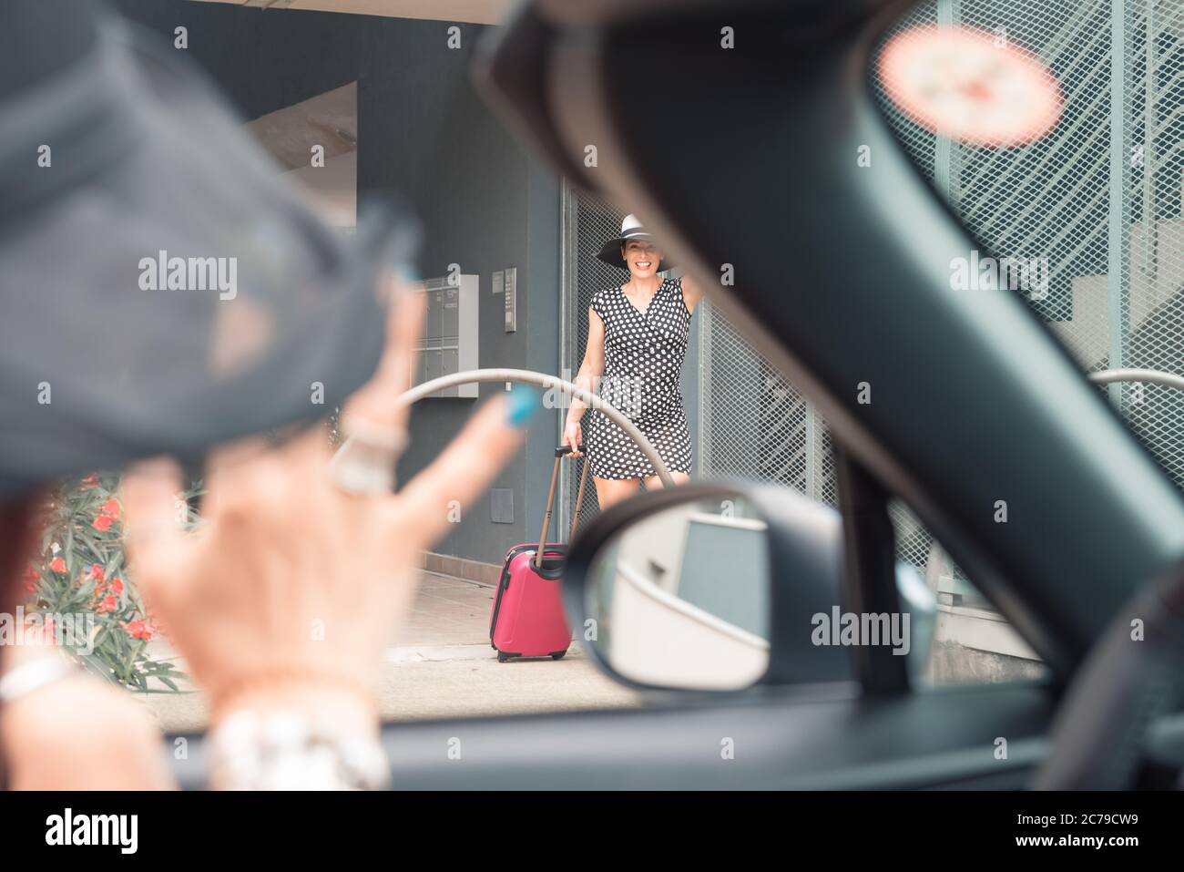 Elegante donna in mini abito con alte tacche che cammina verso l'auto con la valigia. Foto Stock