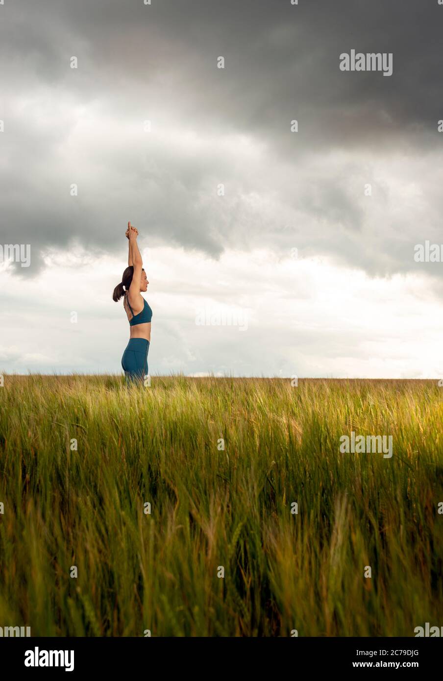 Donna che pratica yoga e meditazione in un campo, cielo drammatico. Foto Stock