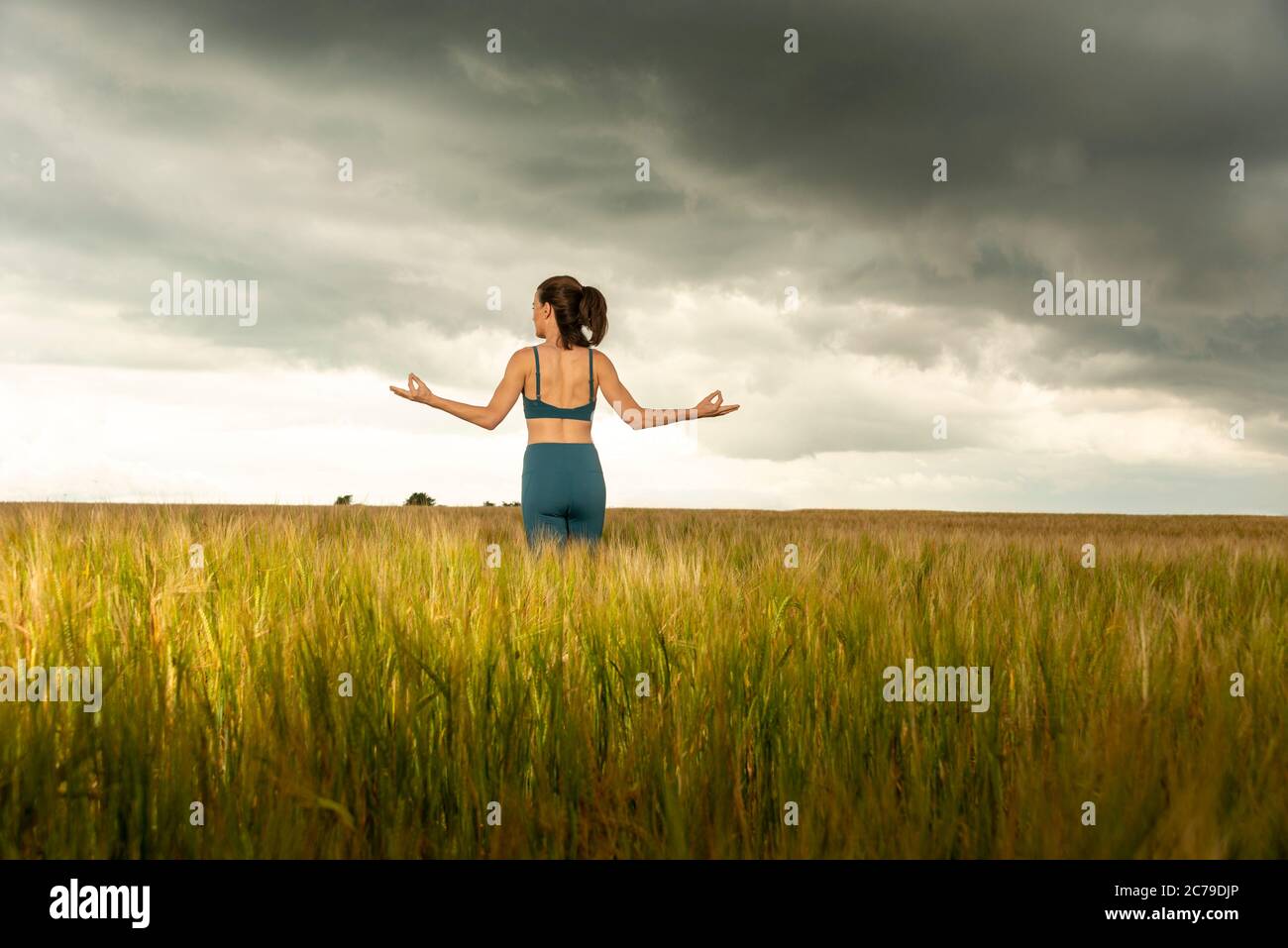 donna che si esercita e medita in un campo di grano con un cielo drammatico tempestoso, Foto Stock