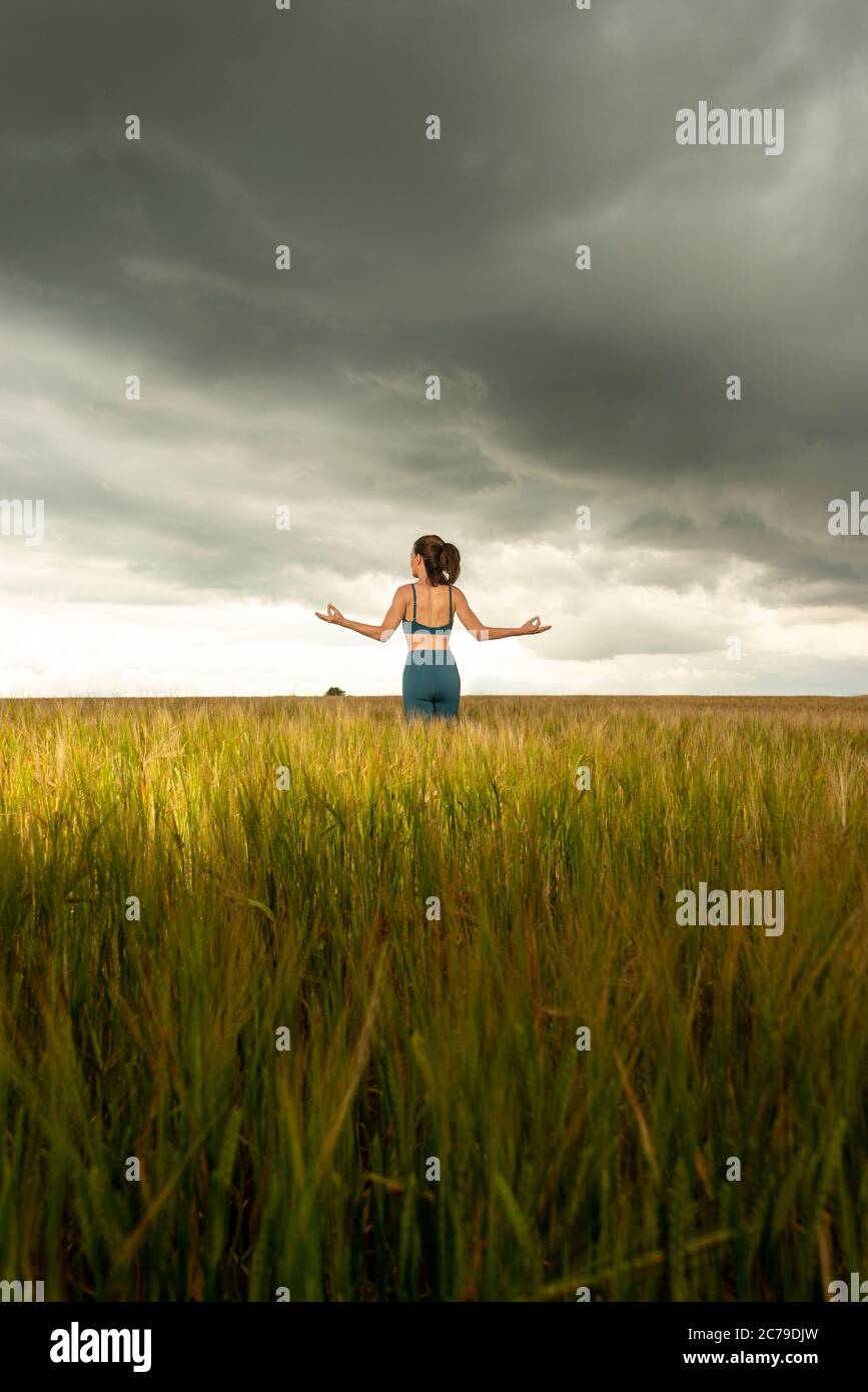 Donna che si esercita e medita in un campo di grano con un cielo drammatico tempestoso, Foto Stock