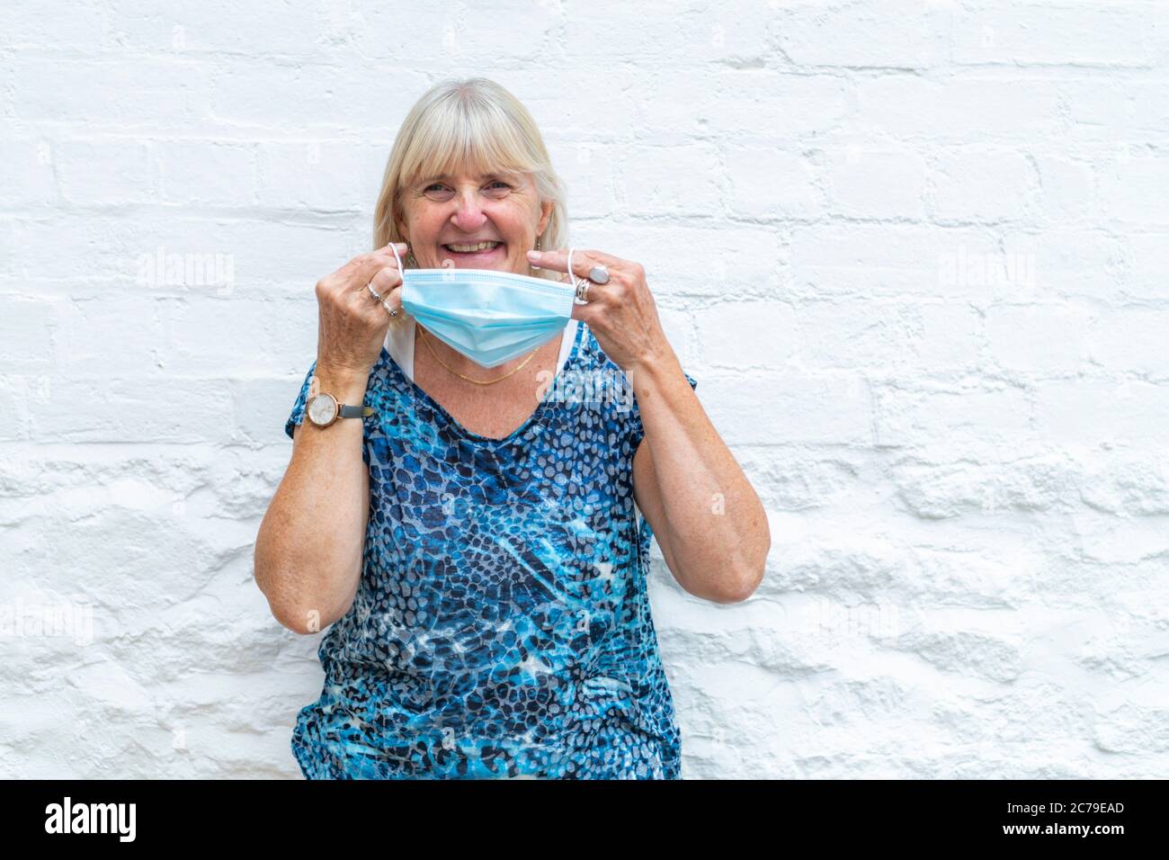 Donna sorridente, indossando una maschera Coronavirus, pandemia Covid-19, pronta per la fine del blocco, indossando quando fuori in pubblico. Sfondo bianco chiaro. Foto Stock