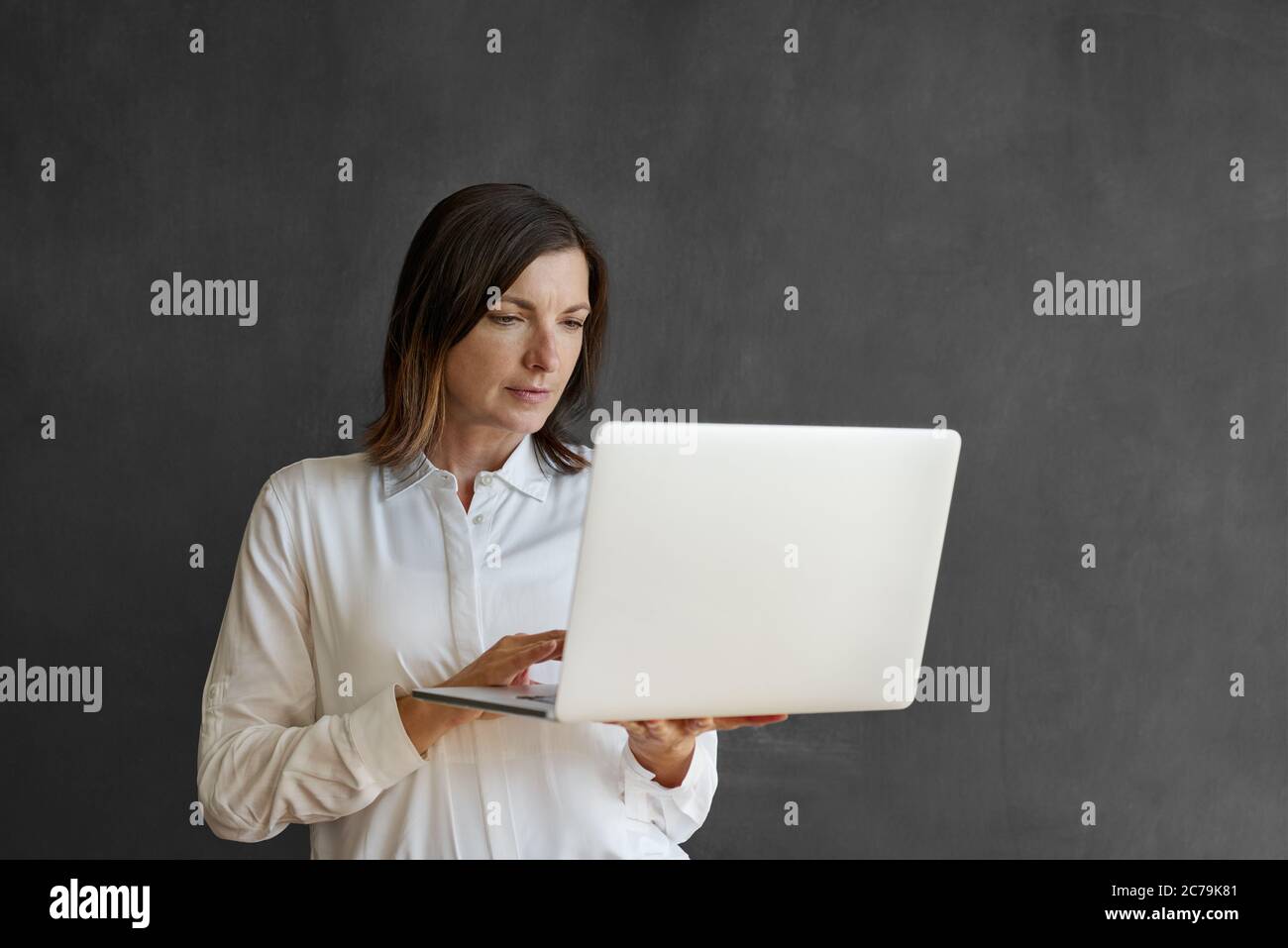 Donna d'affari che lavora su un computer portatile che sta tenendo in piedi davanti a una lavagna bianca Foto Stock