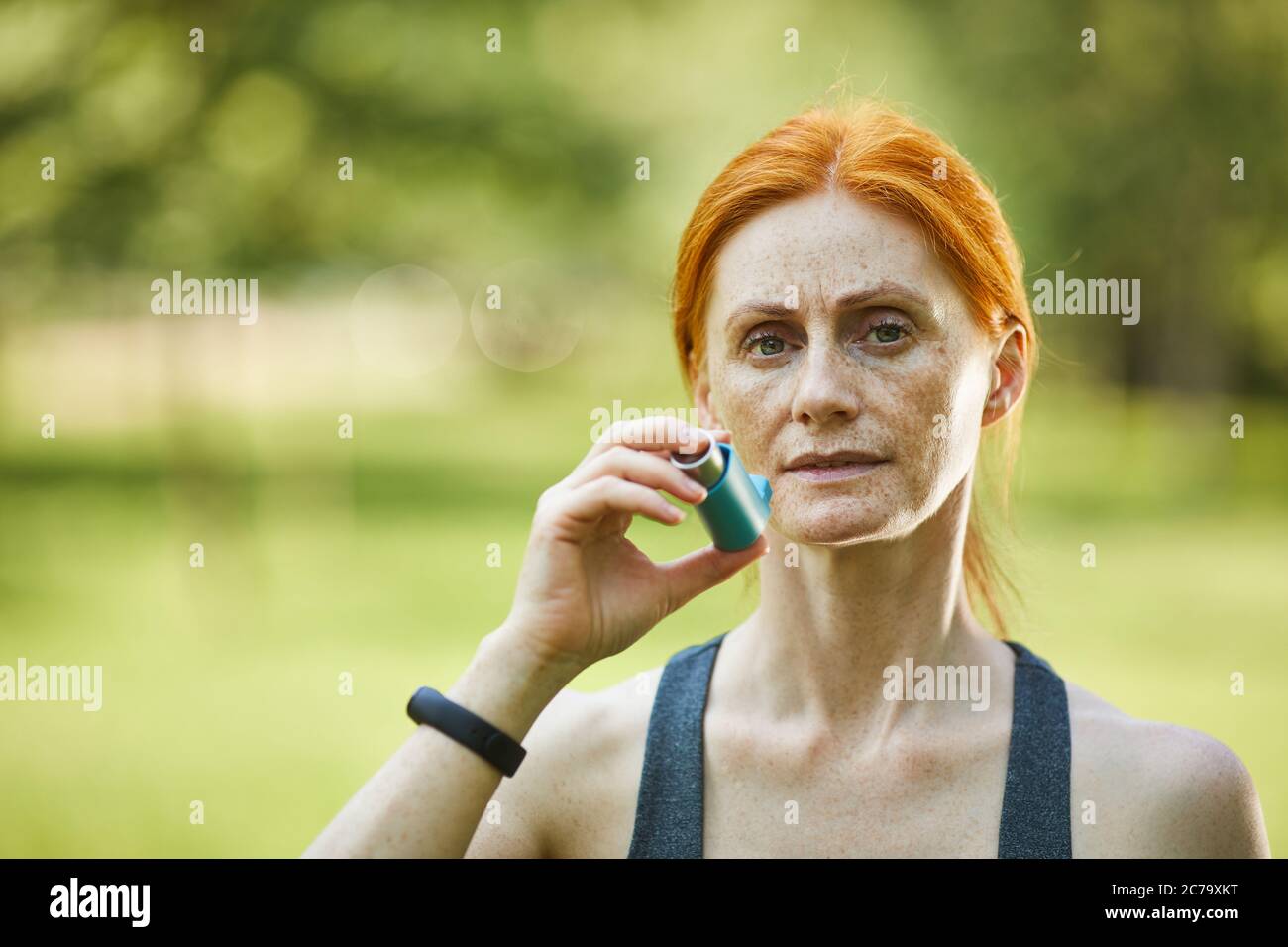 Ritratto di una donna matura gravemente incatenata che usa un inalatore per prevenire l'attacco di asma dopo l'allenamento nel parco Foto Stock