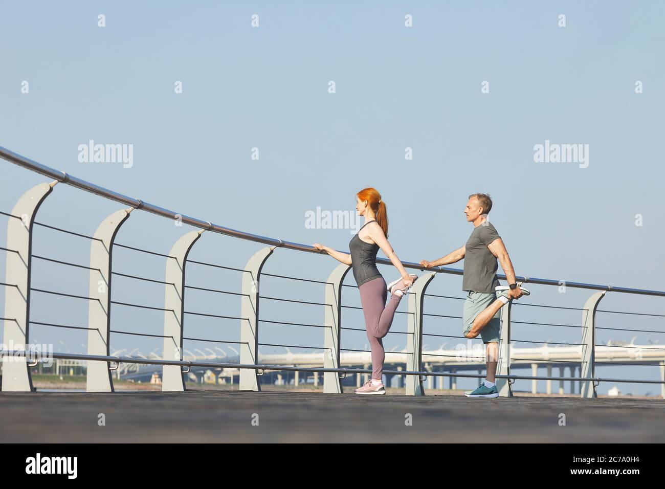 Coppia sportiva matura in piedi su ringhiera e gambe stretching mentre si allenano insieme Foto Stock