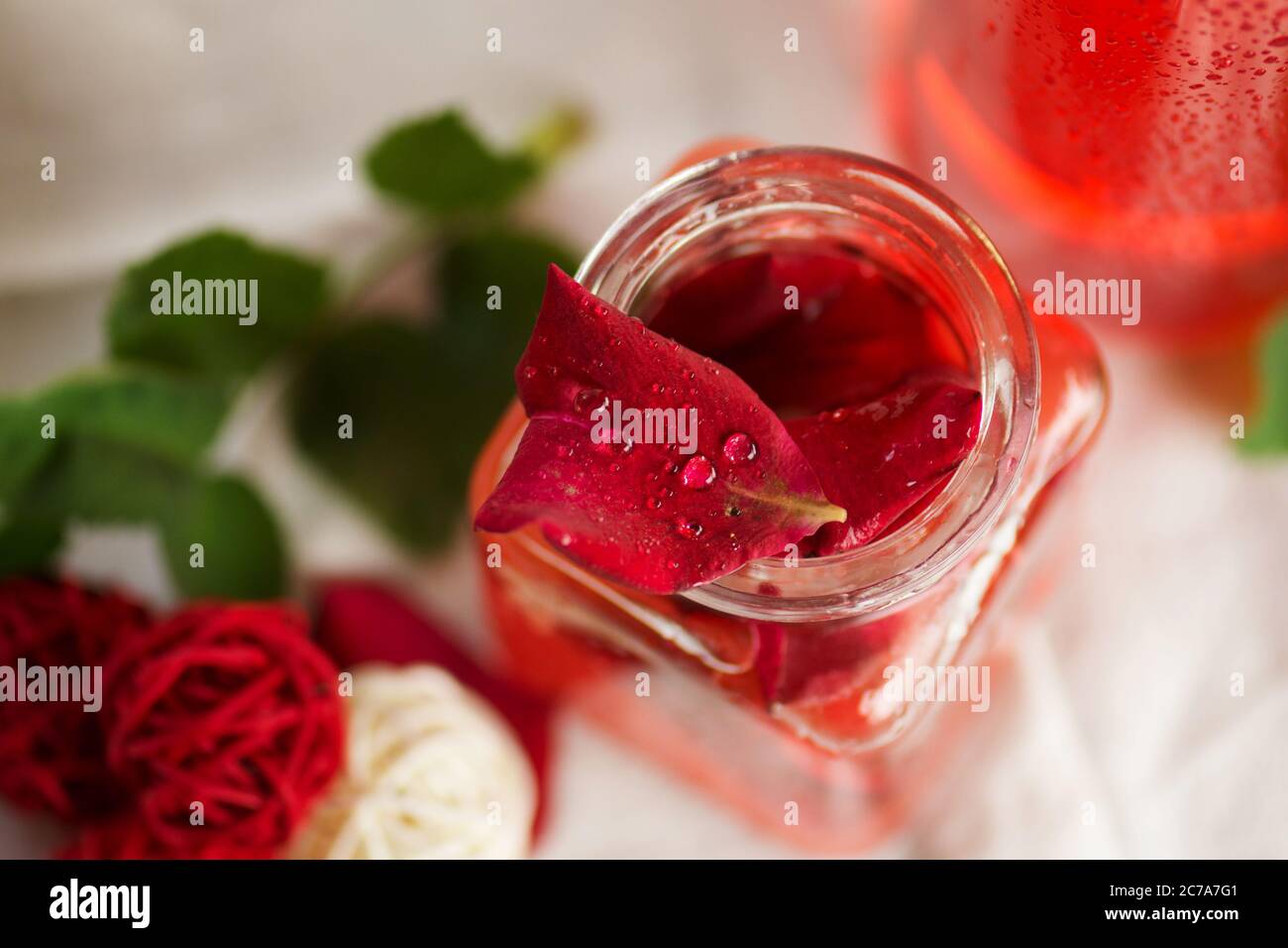 Acqua profumata di rose. Set benessere con olio di petali di rosa. Rosa fiore e bicchiere di acqua di rosa. Acqua di rose organica fresca Foto Stock