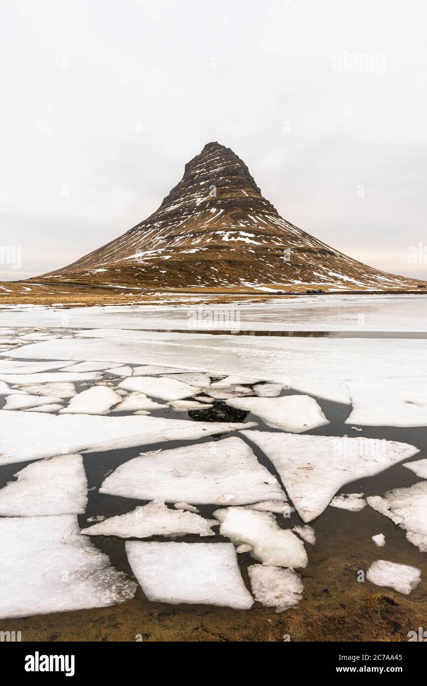 Kirkjufell sopra i fogli di ghiaccio che galleggiano sulla laguna di marea. Foto Stock