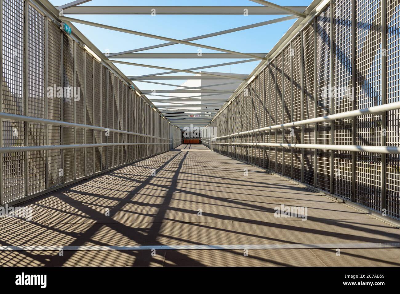 All'interno di un moderno ponte pedonale sopra una superstrada in una giornata di sole. Riduzione della prospettiva e delle ombre dalla recinzione sul pavimento. Foto Stock