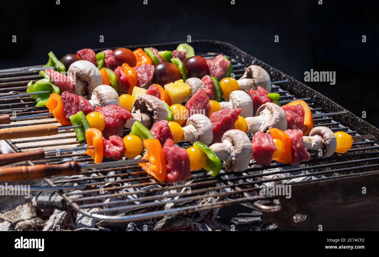 Spiedini grigliati di verdure e carne alla griglia all'aperto. Carbone visibile incandescente. Foto Stock
