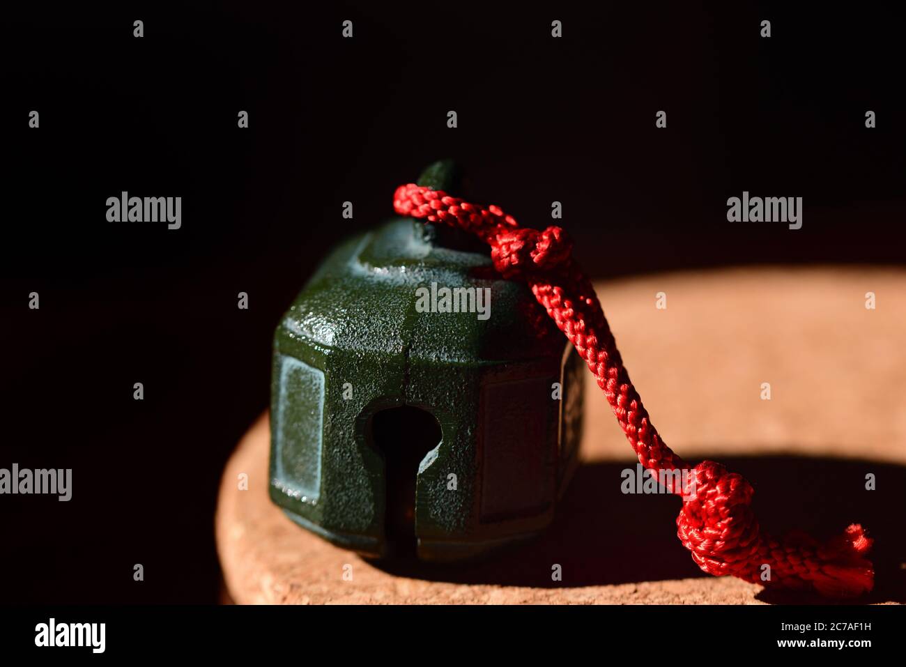 Su una piastra rotonda in sughero si trova una campana verde di metallo, con una corda rossa su di essa, su uno sfondo scuro Foto Stock