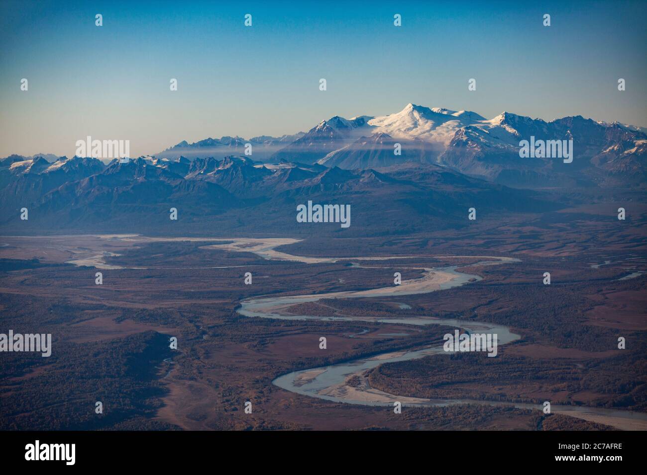 Una vista aerea di un fiume tortuoso che scorre attraverso la vasta natura selvaggia dell'Alaska, incorniciata da montagne innevate sotto un cielo azzurro. Foto Stock