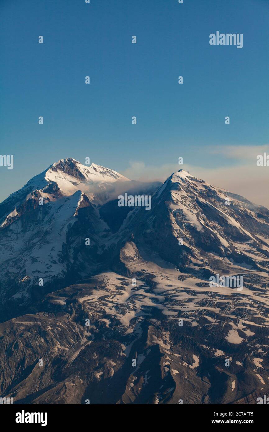 Montagna vulcanica innevata con un pennacchio di fumo che scorre attraverso il cielo, mostrando il suggestivo e aspro paesaggio selvaggio dell'Alaska. Foto Stock