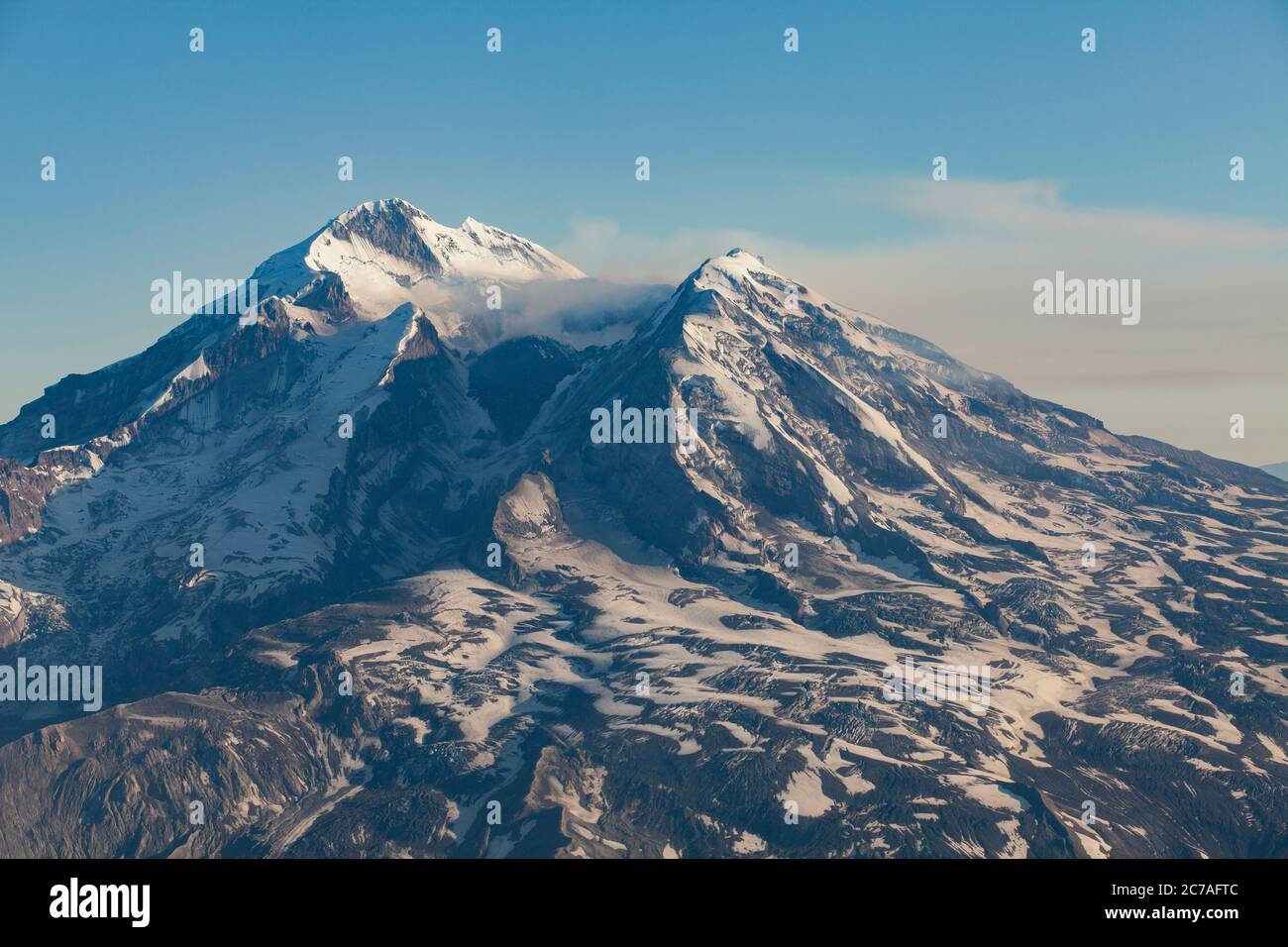 Montagna vulcanica innevata con un pennacchio di fumo che scorre attraverso il cielo, mostrando il suggestivo e aspro paesaggio selvaggio dell'Alaska. Foto Stock