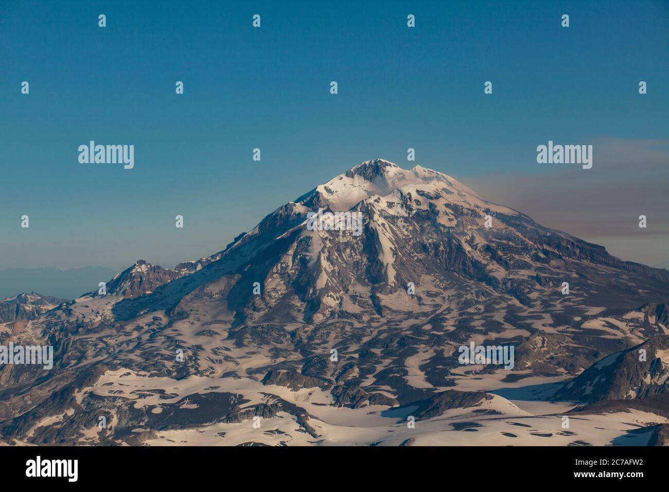 Montagna vulcanica innevata con un pennacchio di fumo che scorre attraverso il cielo, mostrando il suggestivo e aspro paesaggio selvaggio dell'Alaska. Foto Stock