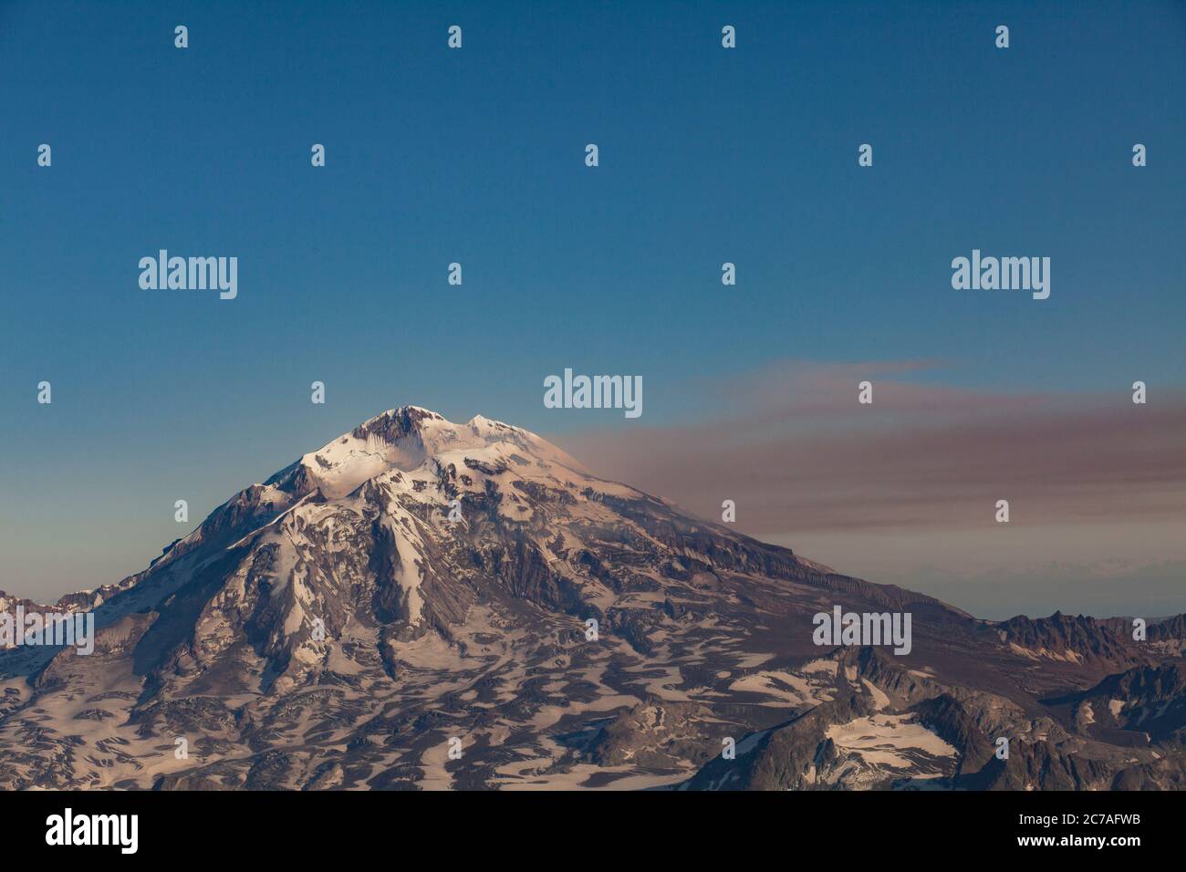 Montagna vulcanica innevata con un pennacchio di fumo che scorre attraverso il cielo, mostrando il suggestivo e aspro paesaggio selvaggio dell'Alaska. Foto Stock