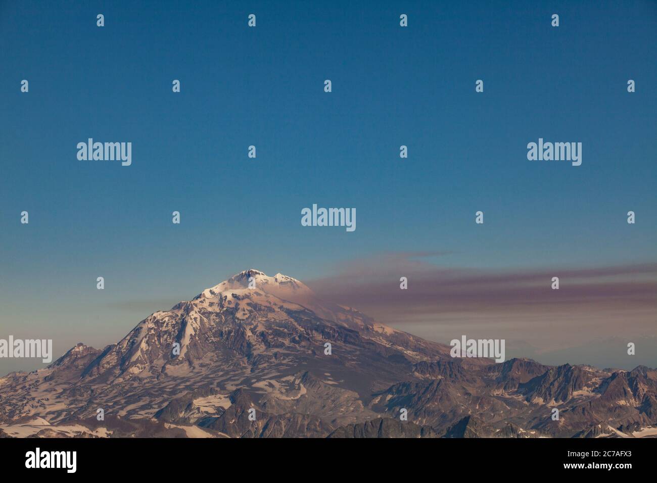 Montagna vulcanica innevata con un pennacchio di fumo che scorre attraverso il cielo, mostrando il suggestivo e aspro paesaggio selvaggio dell'Alaska. Foto Stock
