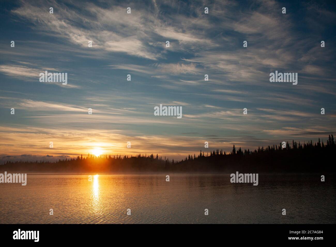 Tramonto dorato su un lago dell'Alaska, con sagome di montagna e morbide nuvole che riflettono la serena bellezza della natura selvaggia durante il crepuscolo. Foto Stock