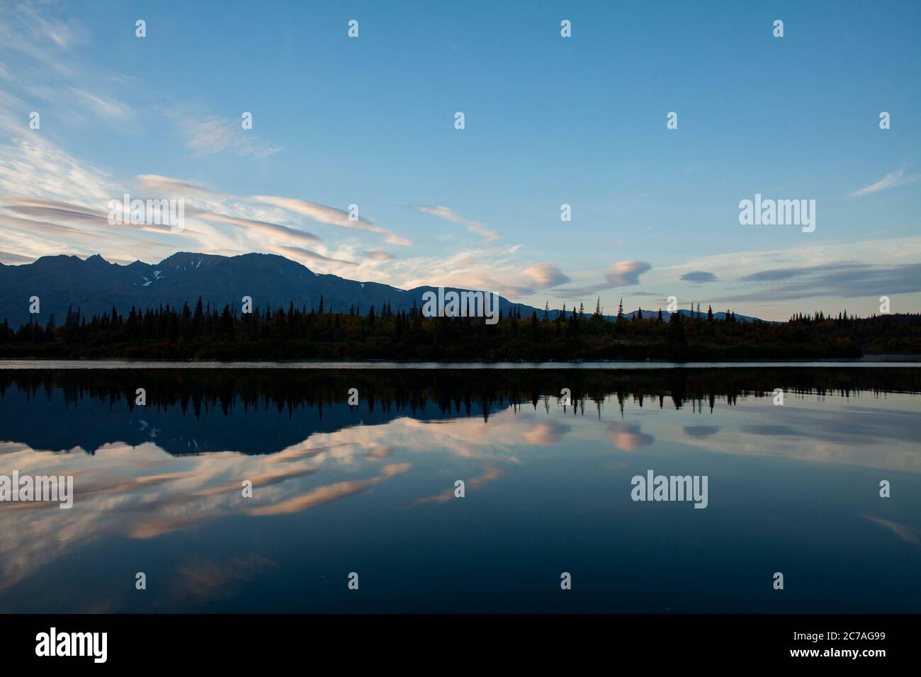 Riflessi di nuvole e sagome di montagna su un tranquillo lago dell'Alaska durante il crepuscolo, catturando la serena bellezza della natura incontaminata. Foto Stock