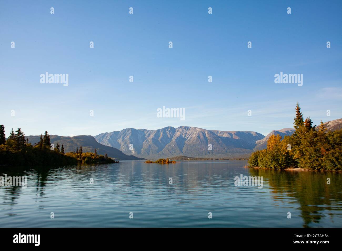 Lago incontaminato dell'Alaska con acque calme e riflettenti che rispecchiano aspre montagne sotto un cielo limpido, catturando la serenità incontaminata della natura selvaggia. Foto Stock
