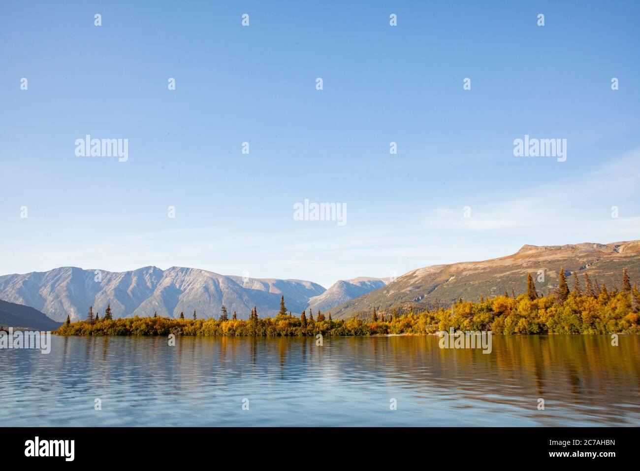 Lago incontaminato dell'Alaska con acque calme e riflettenti che rispecchiano aspre montagne sotto un cielo limpido, catturando la serenità incontaminata della natura selvaggia. Foto Stock