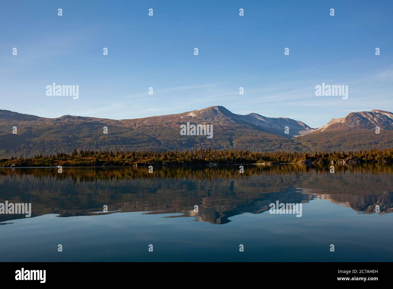 Lago incontaminato dell'Alaska con acque calme e riflettenti che rispecchiano aspre montagne sotto un cielo limpido, catturando la serenità incontaminata della natura selvaggia. Foto Stock