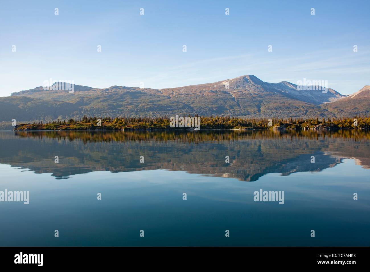 Lago incontaminato dell'Alaska con acque calme e riflettenti che rispecchiano aspre montagne sotto un cielo limpido, catturando la serenità incontaminata della natura selvaggia. Foto Stock