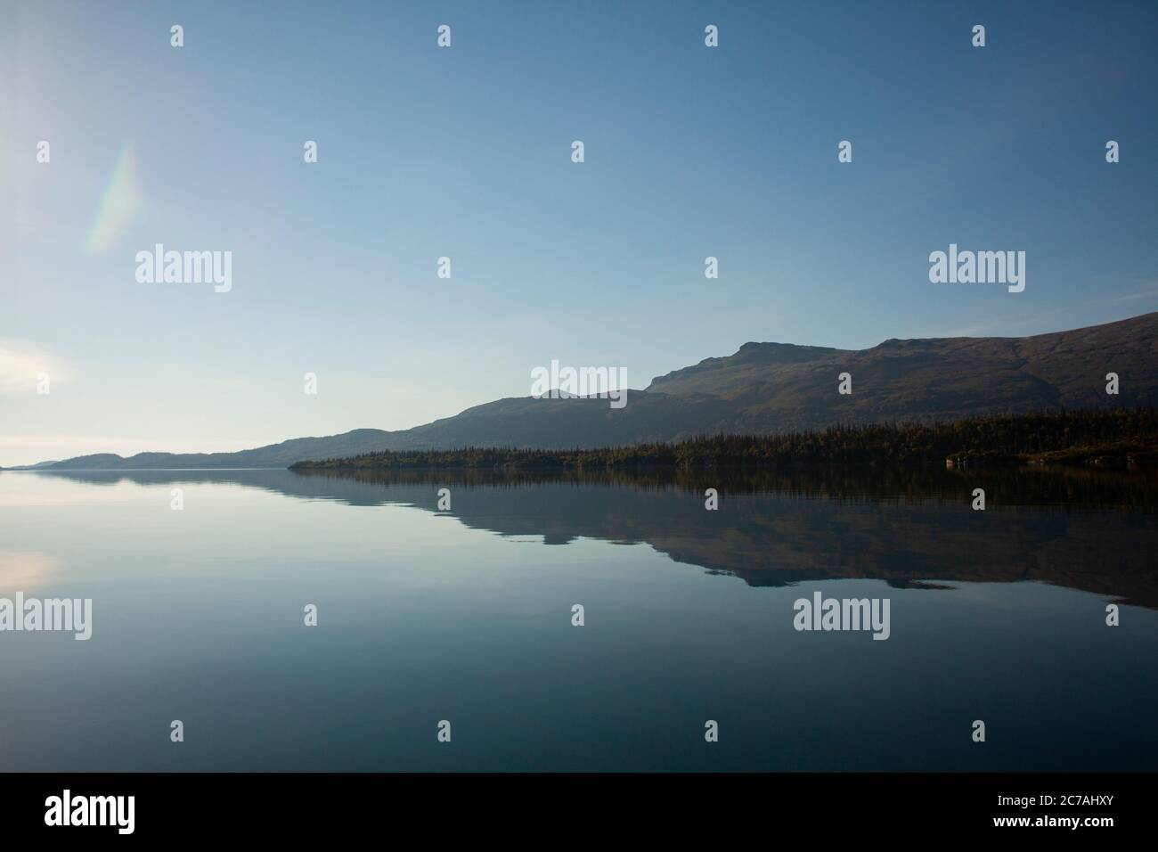 Lago incontaminato dell'Alaska con acque calme e riflettenti che rispecchiano aspre montagne sotto un cielo limpido, catturando la serenità incontaminata della natura selvaggia. Foto Stock