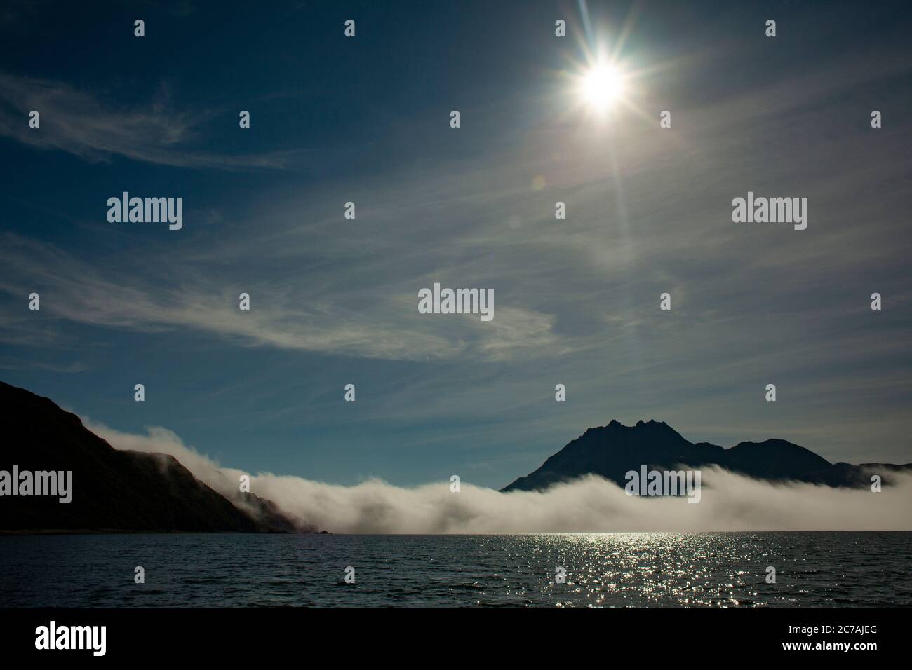 La nebbia si snoda sulle acque del lago Iliamna, Alaska, con il sole che getta luce sull'aspra silhouette di montagna e sul tranquillo paesaggio selvaggio Foto Stock