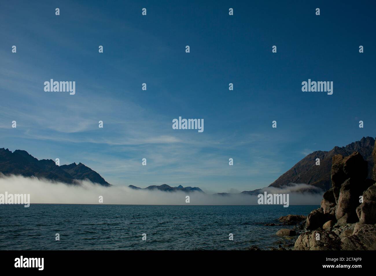 La nebbia si snoda sulle acque del lago Iliamna, Alaska, con il sole che getta luce sull'aspra silhouette di montagna e sul tranquillo paesaggio selvaggio Foto Stock