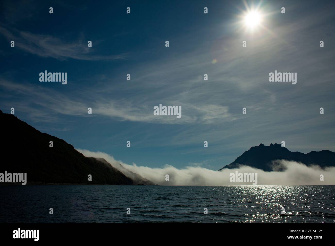La nebbia si snoda sulle acque del lago Iliamna, Alaska, con il sole che getta luce sull'aspra silhouette di montagna e sul tranquillo paesaggio selvaggio Foto Stock